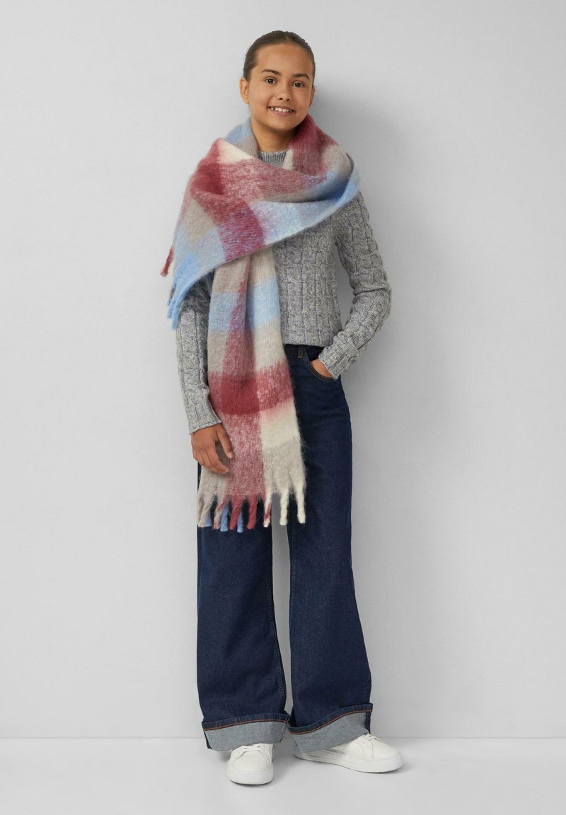 Gestreifter Schal aus weichem Wollmix in den Farben Rot, Blau und Beige. Fransen an den Rändern sorgen für Textur. Das Modell trägt einen grauen Pullover und Jeans.
