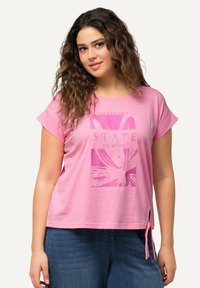 Růžové tričko s krátkým rukávem, které má květinovou grafiku a text "LETO JE STAV MYSLI." Doplňují ho boční šňůrky na lemu pro přidaný detail.