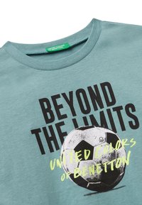 Türkisfarbene Baumwoll-T-Shirt mit Rundhalsausschnitt, auffälligem schwarzen Druck mit der Aufschrift "BEYOND THE LIMITS" und einem grafischen Fußball, verziert mit limettengrünen Akzenten.