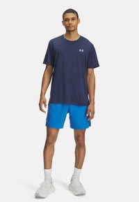 Mörkblå kortärmad sporttröja i textil, i kombination med ljusblå shorts och vita sportskor med texturerade sulor.