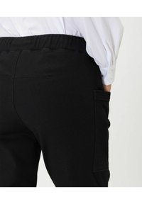 Pantalones negros con una cinturilla elástica y un bolsillo lateral, con una textura de tela suave y diseño ajustado, mostrados desde la parte de atrás.