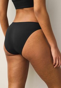Zwarte hooggewaist bikini onderkant gemaakt van soepel, rekbaar materiaal. Kenmerkt zich door een naadloos ontwerp met minimale bedekking en een lichte glans.