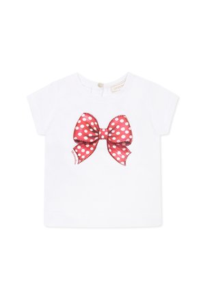 T-shirt bianco a maniche corte con una grande grafica di un fiocco rosso a pois al centro. Materiale in cotone morbido con chiusura a bottoni sul retro.