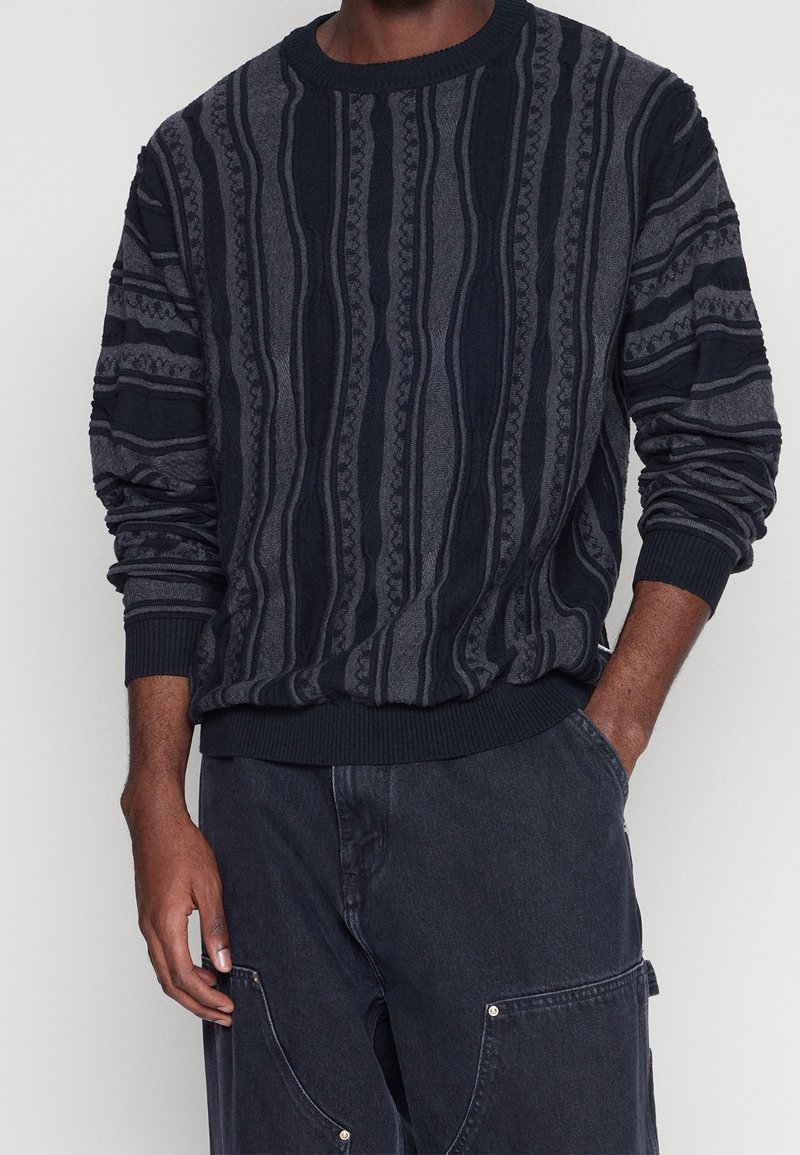 Pletený svetr v námořnické modři a šedé barvě s texturovaným pruhovaným vzorem. Má žebrované manžety a lem. Vyrobený z měkkého pleteného materiálu.