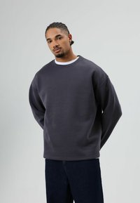 Donkergrijze sweatshirt met een vrije pasvorm, ronde halslijn en lange mouwen, gecombineerd met een donkere spijkerbroek. Soepele textuur en eenvoudig ontwerp.