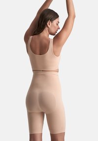 Set di shapewear beige composto da una maglietta senza maniche e pantaloni corti a metà coscia, realizzato in un tessuto liscio e elasticizzato con una vestibilità aderente.