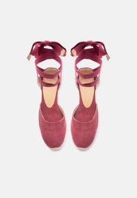 Κόκκινα υφασμάτινα εσπαντρίγιες με κορδόνια δέσιμο στον αστράγαλο και πλεκτές σόλες από τσόχινη ίνα, εμφανιζόμενα από ψηλά σε λευκό φόντο.