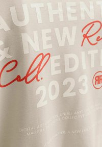 Λευκό ύφασμα με εκρού και κόκκινο κείμενο που γράφει «Authentic New Edition 2023 Coll.», συν μικρότερο περιγραφικό κείμενο για την ψηφιακή καλλιτεχνική διεύθυνση.