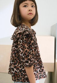 Haut imprimé léopard avec décolleté froncé et manches bouffantes, comportant des nuances de marron, noir et crème, fabriqué en tissu léger.