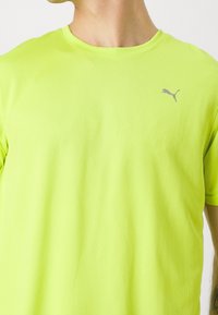 Camiseta de manga corta amarilla brillante, hecha de un tejido texturizado, que presenta un pequeño logo gris de Puma en el pecho. Diseño de cuello redondo.