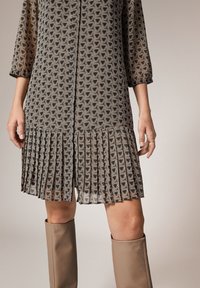 Robe à motifs avec un design géométrique en marron et crème. Le tissu a un ourlet plissé et des manches trois-quarts.