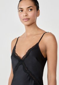 Camisole nera in satin con delicata rifinitura in pizzo nero lungo il scollo a forma di V, dotata di spalline sottili e regolabili.