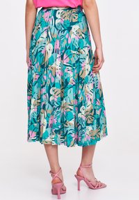 Falbaniasta, turkusowa spódnica z kolorowymi wzorami liści, sięgająca kostek. Noszona z różowymi sandałami na wysokim obcasie z paskami.