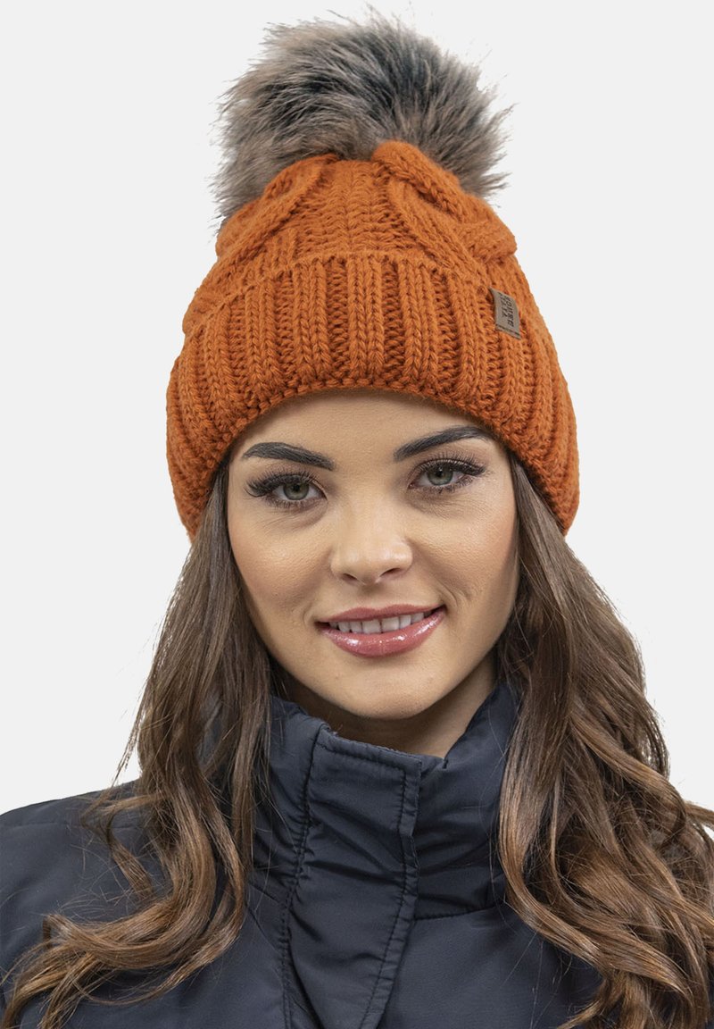 Beanie di maglia arancione con un motivo testurizzato e una pom-pom in pelliccia sintetica sulla parte superiore. Presenta un piccolo etichetta marrone sul lato.