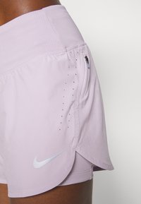 Pantaloni sportivi lilla realizzati in tessuto leggero, con una tasca laterale con zip, un logo Nike argentato e perforazioni ventilate.
