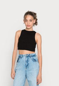 Top preto curto sem mangas com decote redondo, combinado com jeans de cintura alta em azul claro, apresentando bolsos frontais e uma textura desgastada.