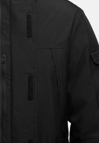 Zwarte jas met ritssluiting, klittenbandaccenten en stikseldetails. Bevat zijzakken en een gestructureerde kraag.