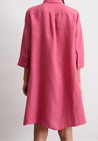Różowa sukienka koszulowa z lnu z kołnierzykiem, długimi rękawami i mankietami na guziki. Posiada luźny krój i gładką fakturę.