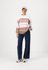 Chunky knit sweater with pink, white, and brown stripes, paired with wide-leg blue denim jeans and beige sneakers. Accessories include a pink cap.