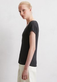T-shirt noir à manches courtes en tissu doux, avec une coupe décontractée et un col rond. Le modèle le porte avec un pantalon clair.