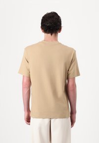 Beige Baumwoll-T-Shirt mit kurzen Ärmeln, Rundhalsausschnitt und lockerer Passform, das eine glatte Textur und ein minimalistisches Design aufweist.