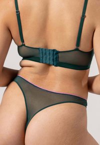 Teal verkko rintaliivit säädettävillä olkaimilla ja hakaskiinnityksellä, yhdistettynä teal väriseen thong-pantyyn, jossa on vaaleanpunaiset yksityiskohdat. Liukas pinta, jossa on minimaalinen peittävyys.