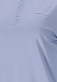Helles blaues Sportshirt mit einem Viertelreißverschluss-Design. Es hat eine dezente Textur und ist mit "ENDURANCE" in unauffälliger Schrift versehen.