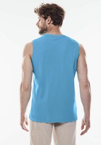 Ärmlös blå bomullstopp, lättviktsmaterial, rundad halsringning, rak fåll och synliga sömmar på ryggen.