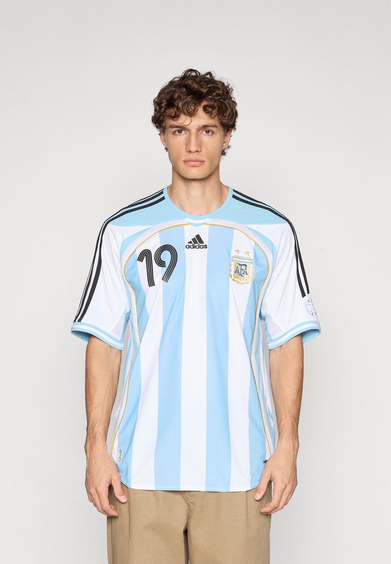 Η φανέλα της εθνικής ομάδας ποδοσφαίρου της Αργεντινής με κάθετες ριγες σε γαλάζιο και λευκό. Μαύρες ρίγες Adidas στα μανίκια και λογότυπο· αριθμός παίκτη 19.