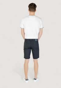 Camicia bianca a maniche corte con bordi neri, abbinata a pantaloni corti scuri e scarpe bianche. Cuciture e tasche visibili sui pantaloni.