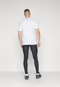 Bílé tričko s krátkým rukávem, černé legíny a šedé sportovní boty s oranžovými detaily. Hladká textura a přiléhavý design, zobrazeno zezadu.