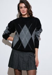 Zwarte en grijze argyle-gepatenteerde trui met geribbelde manchetten, gecombineerd met een geplooide antracietrok. Gladde textuur, casual pasvorm en ronde halslijn.