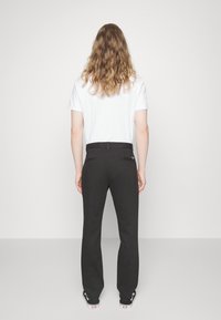 Pantaloni neri con design a gamba dritta e tasche posteriori, abbinati a una t-shirt bianca a maniche corte, indossati con sneaker nere.