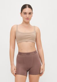 Bežani rebrasti crop top s tankim trakama i UGG logotipom. Smešasti bokser šortsevi s elastičnim pojasom, vidljivim šavovima. Jednostavan, prilagođen dizajn.