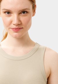 Top a canotta beige a costine con scollatura rotonda e bretelle strette, superficie strutturata, design aderente e dettagli di cucitura sottili.