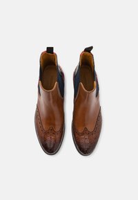 Bottes ankle en cuir marron avec un dessus lisse, un bout texturé contrastant, des panneaux latéraux élastiques et des détails de couture décoratifs.