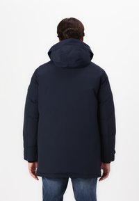 Giacca a vento blu navy con cappuccio, di tipo imbottito, dal tessuto liscio, con una vestibilità rilassata e maniche lunghe. Vista posteriore con dettagli minimi.
