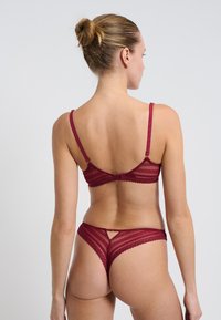 Set di reggiseno e perizoma in pizzo bordeaux con design a cinturino, bordi ondulati e dettaglio a chiave sul retro del perizoma.