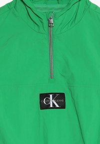 Zielona bluza z lekkiego materiału. Posiada pół-zamek, regulowany kaptur oraz naszywkę z logotypem "CALVIN KLEIN JEANS".