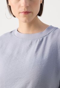 T-shirt en coton violet clair avec un col rond et des manches courtes. Texture lisse, sans motifs ni graphiques visibles. Design simple.