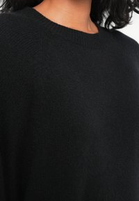 Un pull en tricot noir avec un col rond et un tissu texturé. Gros plan mettant en valeur la douceur et les bords côtelés.
