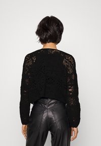 Černý háčkovaný svetr s volným, texturovaným designem a dlouhými rukávy, v kombinaci s přiléhavými černými koženými kalhotami.