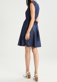 Džínsové šaty s krátkým rukávem, přiléhavým živůtkem a rozšířenou sukni. Mají zavazování na zadní straně, jednotnou tmavě modrou barvu a hladkou strukturu.