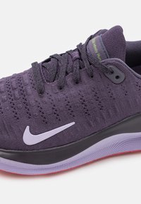 Scarpa da corsa Nike di un viola scuro con tomaia in maglia, intersuola nera, suola esterna viola e accenti grigi; presenta un sistema di allacciatura dinamica e una texture traspirante.