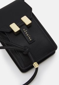 Czarny skórzany portfel o teksturowanym wykończeniu, ze złotymi akcentami, i regulowanym paskiem. Posiada zapięcie na klamrę oraz detal z logo.