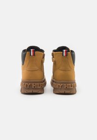 Rudoniams zomšiniai batai iki kulkšnies su juodais akcentais, turintys tekstūruotą gumos padą ir nugarinį logotipo detalizavimą. Raudona, balta ir mėlyna juosta ant kulno.