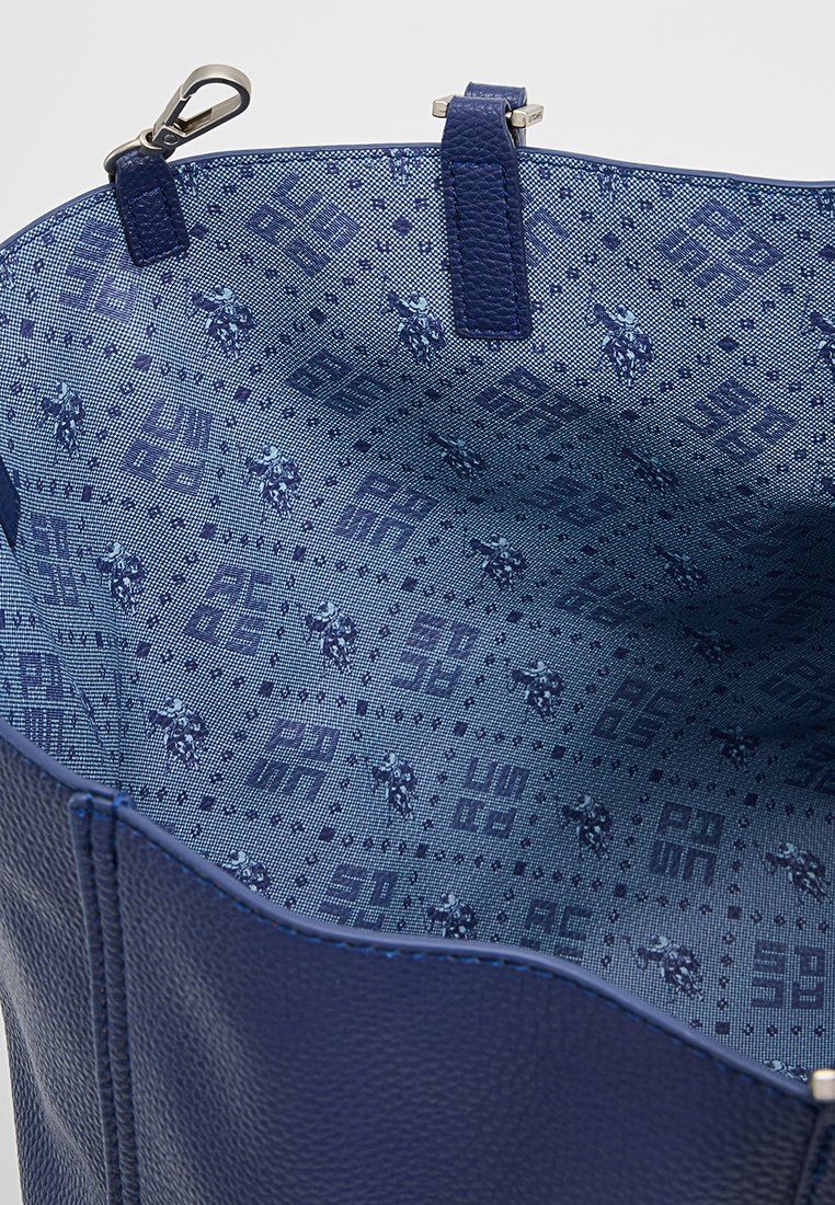 Bolso de mano de cuero azul marino con un exterior texturizado. El interior presenta un forro azul claro de patrones con pequeños motivos y diseños.