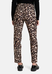 Spodnie w wzór zwierzęcy z beżowym i czarnym wzorem lamparta, zwężane, o wysokim stanie, zestawione z czarnymi, masywnymi butami.