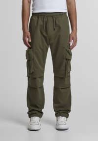 Olive green cargo pants featuring an elastic waistband, multiple side pockets, and a relaxed fit, paired with white sneakers.