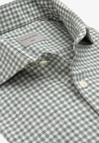 Camicia a maniche corte grigio e bianca a quadri con una texture di tessuto morbido, dotata di colletto con bottoni e piccoli bottoni bianchi. Etichetta del marchio visibile.